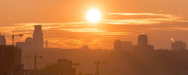 Panoramic view of sunset in the city with silhouette of buildings and industrial cranes