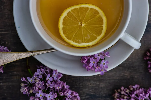 レモンと新鮮なライラックの花をコンクリートの背景にお茶のカップ — ストック写真