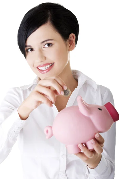 Geschäftsfrau steckt eine Münze in ein Sparschwein — Stockfoto