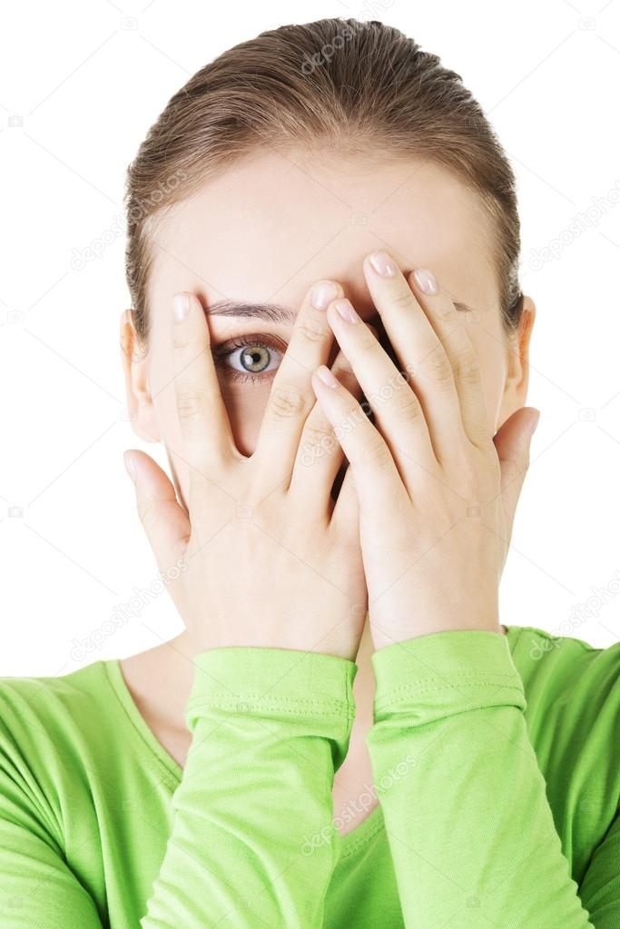 Shy or scared teenage girl peeking through covered face