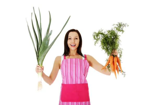Happy woman in apron holding fresh leek and carrot — Stock Photo, Image