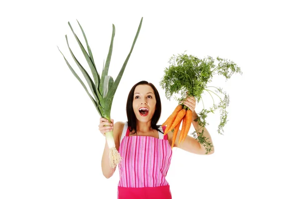 Happy woman in apron holding fresh leek and carrot — Stock Photo, Image