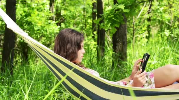 Une femme attrayante couchée dans un hamac avec un ordinateur tablette . — Video