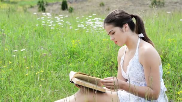 Красивая молодая девушка читает книгу на открытом воздухе — стоковое видео