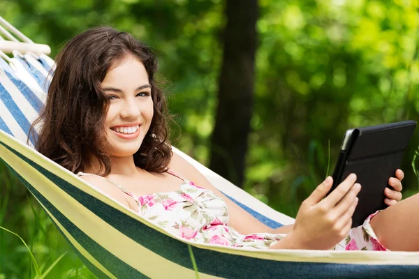 Young woman lying in a hammock in garden with E-Book. — Stock Photo, Image