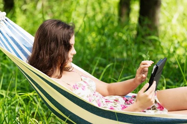 Młoda kobieta leżący w hamaku w ogrodzie z e-book. — Zdjęcie stockowe