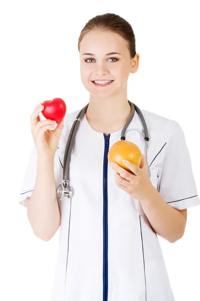 Vrouwelijke arts holding gezonde grapefruit en rood hart. — Stockfoto