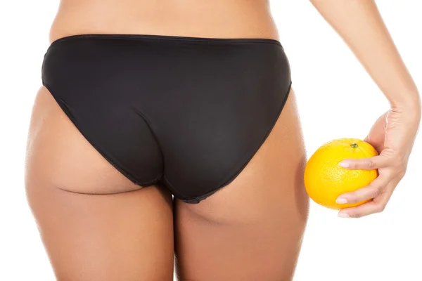 A girl holding an orange next to the buttocks — Stock Photo, Image