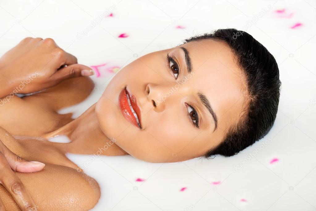 Attractive naked woman lying in a milk bath. With rose petal. Up