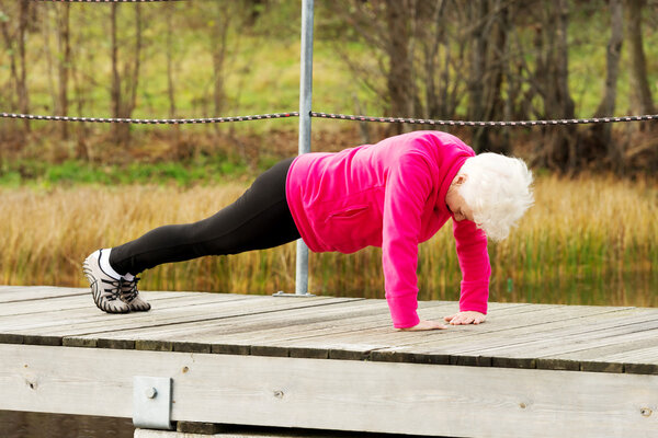 Active grandmum doing push-ups on fresh air.