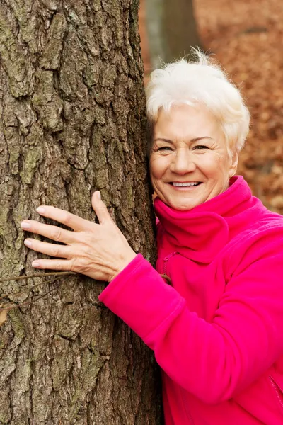 Portrait of an old cherrful lady standing next to a tree. — Stock Photo, Image