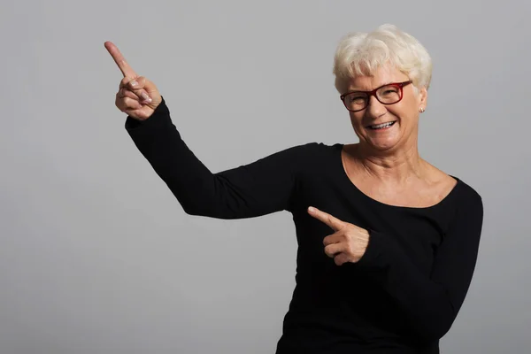 An old happy lady pointing on a copy space. — Stock Photo, Image