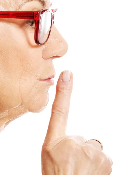Elderly woman is having finger on her lips. Profile. — Stock Photo, Image