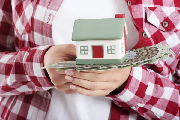 Mulher casual segurando dinheiro e casa a mãos . — Fotografia de Stock