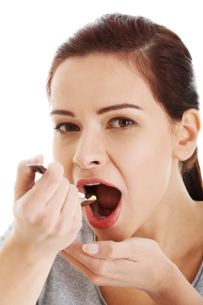 Young casual woman eating pills on a spoon. — Stock Photo, Image