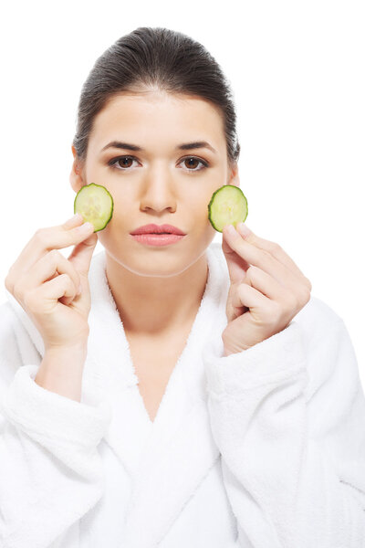 Beautiful woman in bathrobe holding slices of cucumber.