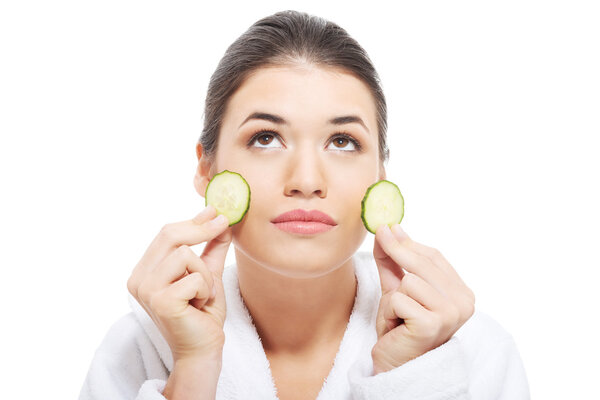 Beautiful woman in bathrobe holding slices of cucumber.