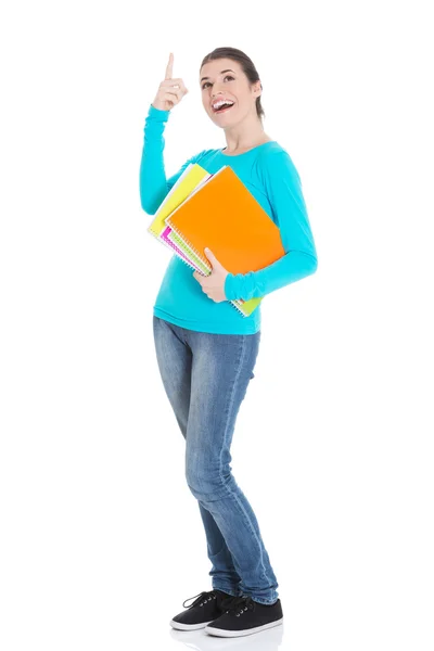 Jovem bela estudante mulher segurando caderno de trabalho e apontando para cima . — Fotografia de Stock