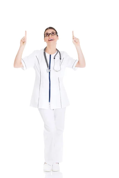 Beautiful young woman doctor pointing up. — Stock Photo, Image