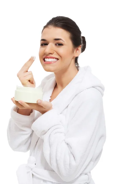 Mooie vrouw in badjas met gezichtscrème. — Stockfoto