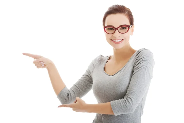 Beautiful casual woman in eyeglasses pointing aside. — Stock Photo, Image