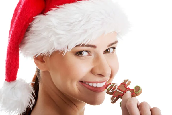 Schöne Frau mit Weihnachtsmannhut isst einen Keks. — Stockfoto