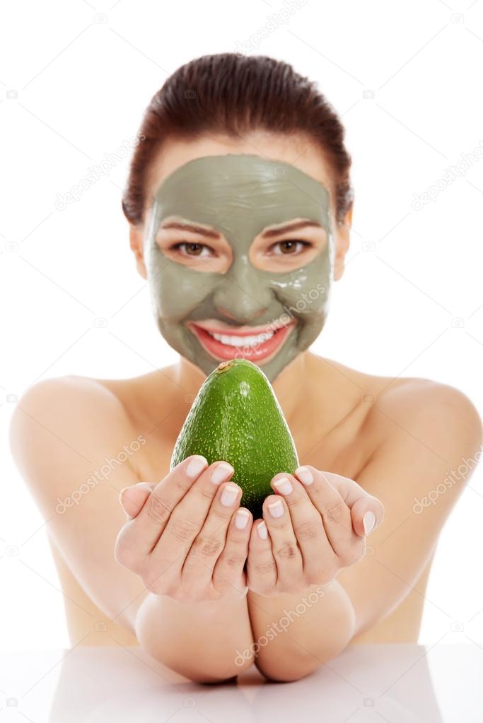 Beautiful woman with facial mask holding avocado.