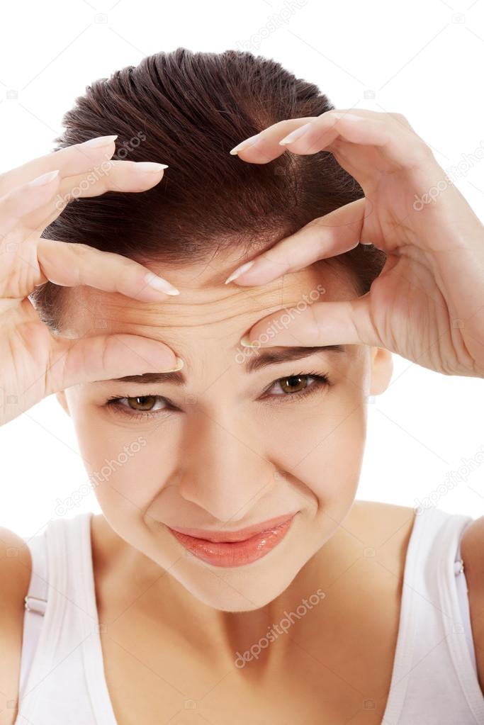 Young beautiful woman is checking her wrinkles on forehead.