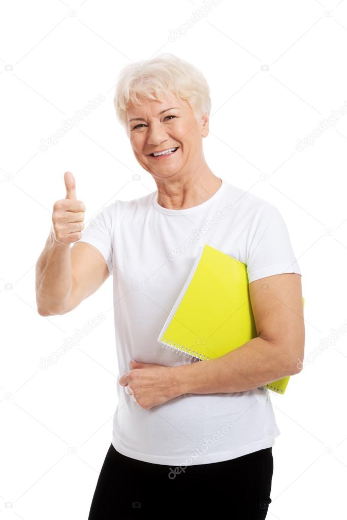 An old woman holding workbook and showing OK.