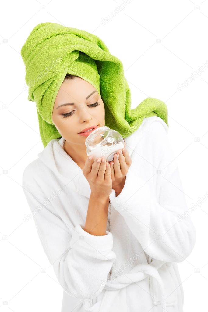 Beautiful woman in bathrobe, turban and holding face cream.