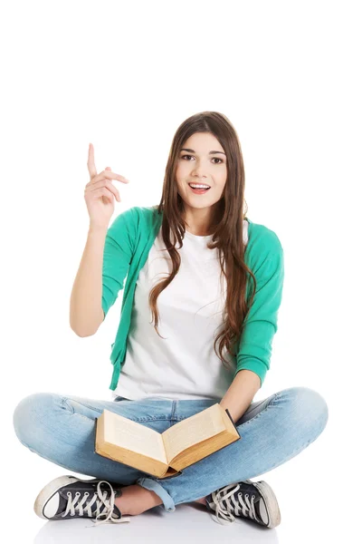 Jovem bela estudante sentada com livro e apontando para cima . — Fotografia de Stock