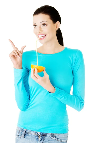 Beautiful young woman drinking juice from orange. — Stock Photo, Image