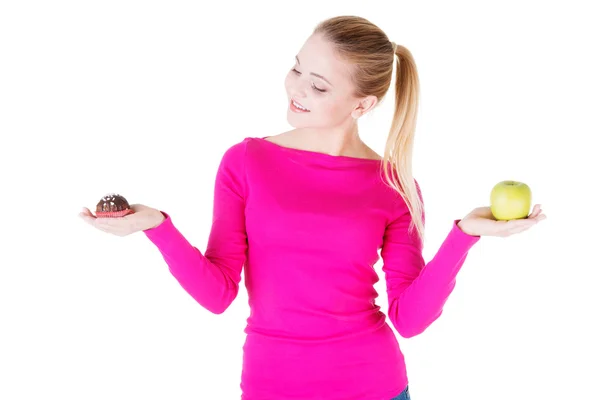 Mladá neformální žena drží jablko a cookie. — Stock fotografie