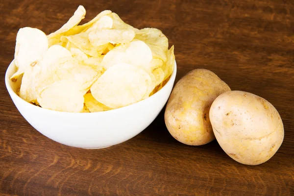 Kartoffelchips in einer Schüssel und Kartoffeln. — Stockfoto