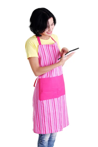 Νεαρή γυναίκα σε ροζ ποδιά χρησιμοποιώντας υπολογιστή δισκίο — Φωτογραφία Αρχείου