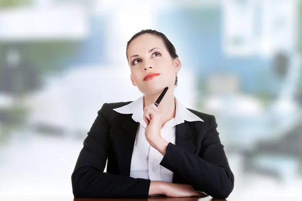 Hübsche Geschäftsfrau sitzt am Schreibtisch und denkt nach — Stockfoto