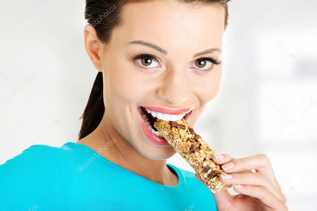 Young woman eating cereal candy bar