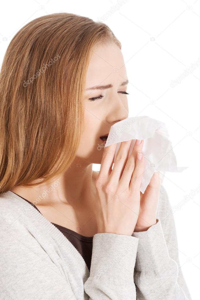 Beautiful woman sneezing, holding a tissue.