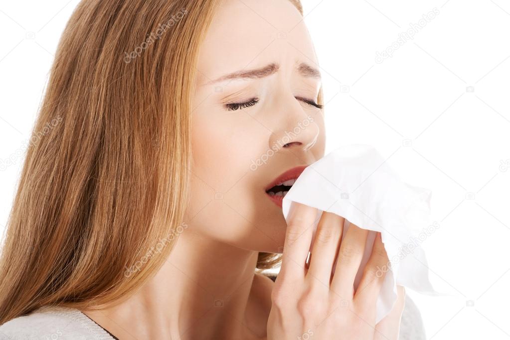 Beautiful woman sneezing, holding a tissue.
