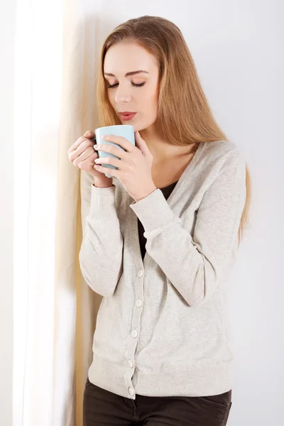 Woman standing by the window with hot drink coffee — Stock Photo, Image