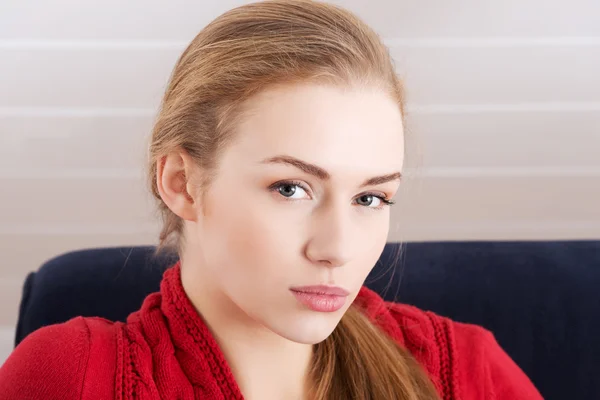 Beautiful caucasian woman sitting ona couch and wearing red pullover — Stock Photo, Image