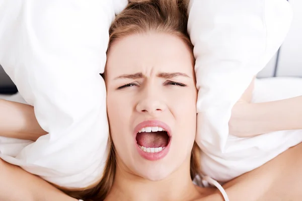 Beautiful business woman lying in bed and covering her ears with pillows — Stock Photo, Image