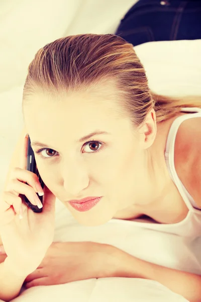 Mooie vrouw met mobiele telefoon liggend op bed — Stockfoto