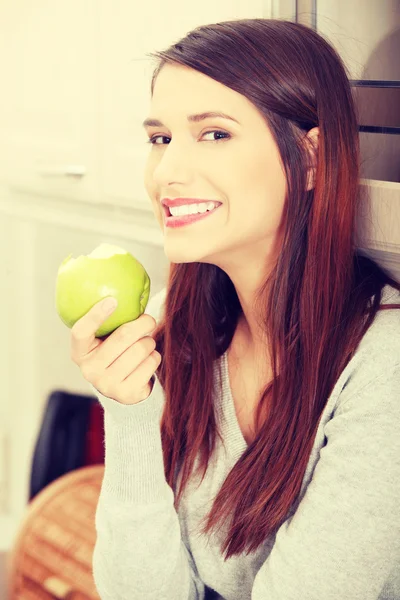 Žena v kuchyni jíst zelené jablko — Stock fotografie