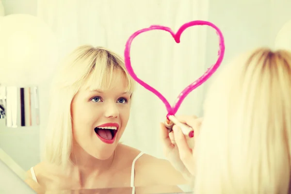 Unga vackra kvinnan ritning stort hjärta på spegel. — Stockfoto