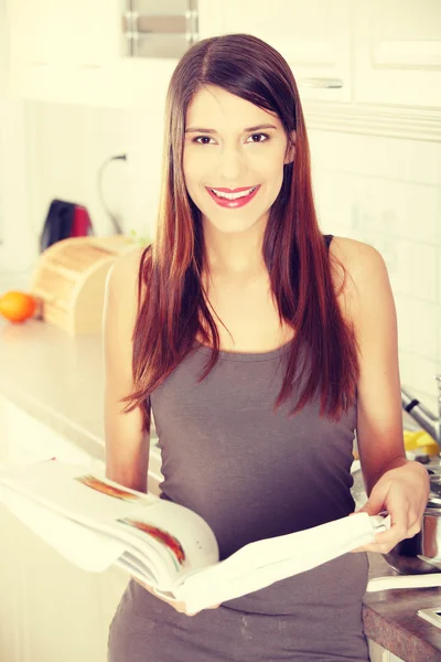 Mladá žena čte kuchařka v kuchyni — Stock fotografie