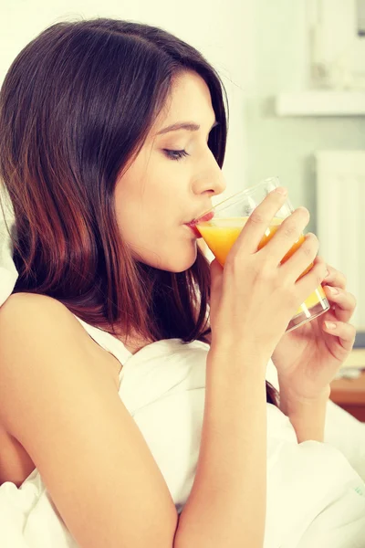 Mulher na cama bebendo suco de laranja — Fotografia de Stock