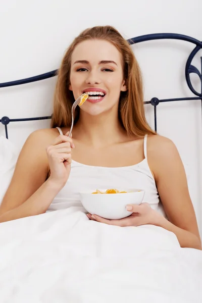 Vacker kaukasisk kvinna äta färsk frukt i sängen. — Stockfoto