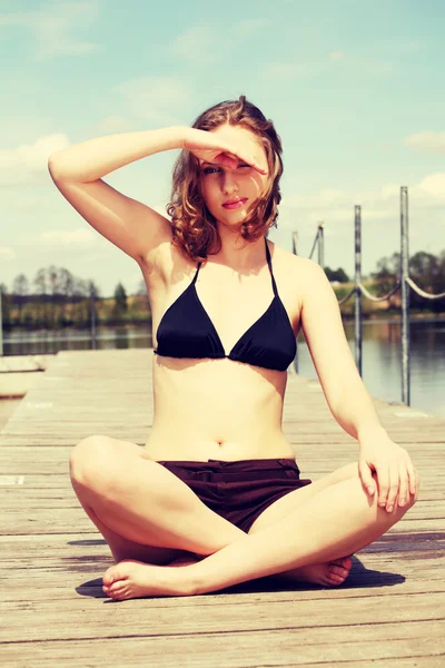 Young woman in bikini is sitting on bridge in sunny day — Stock Photo, Image
