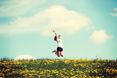 Çiçekli çayırlarda zıplayan kadın.
